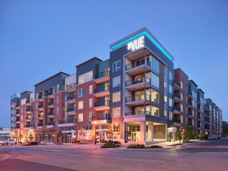 The Vue, a multi-story apartment complex with balconies and retail space on the ground floor, illuminated by soft evening lights.