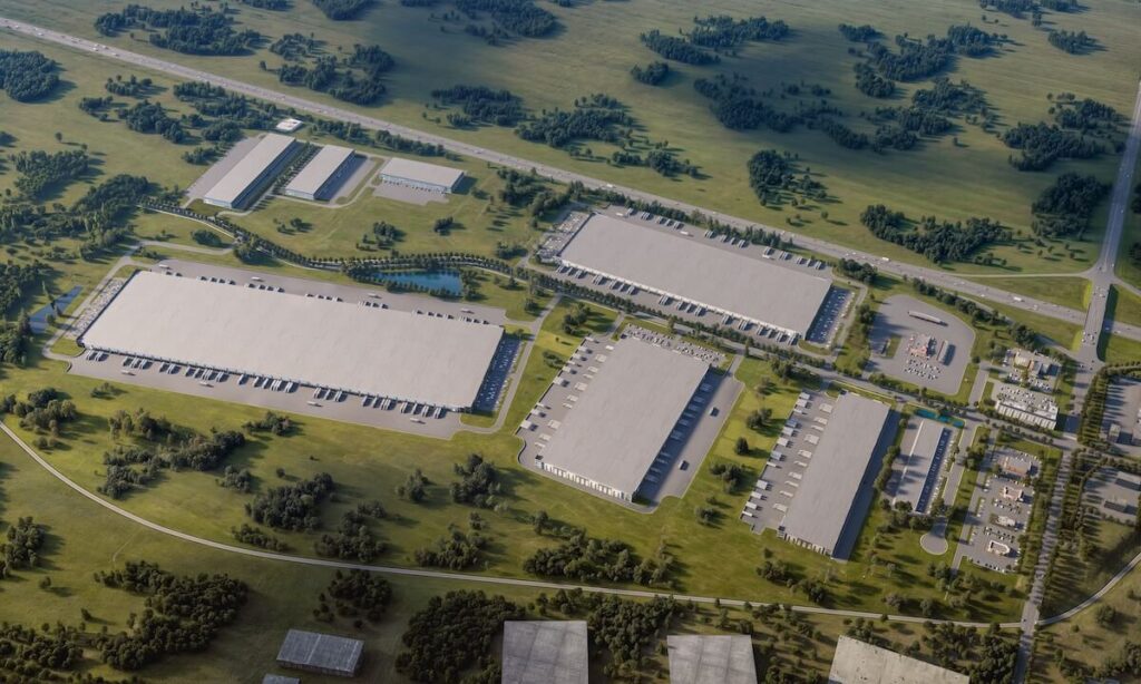 Large industrial park with multiple warehouse buildings, truck docks, parking lots, and surrounding green landscape near a highway.