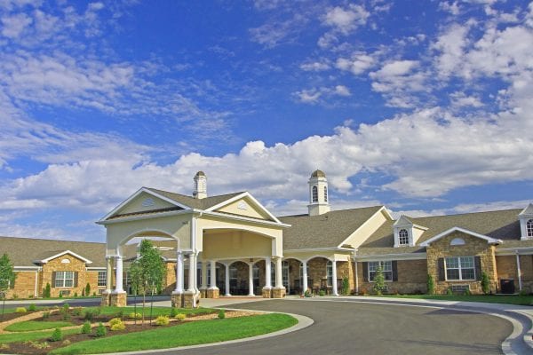 Large brick and stone building with white columns, arched entryway, manicured landscaping, and blue sky backdrop.