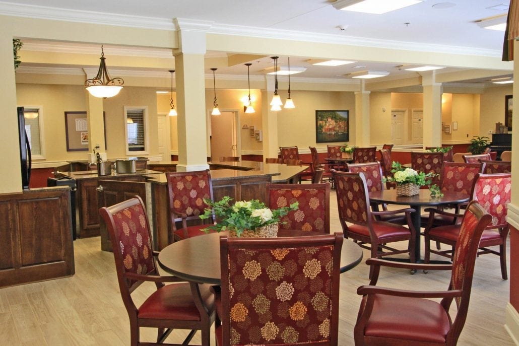 Spacious dining area with round tables, red patterned chairs, pendant lighting, and potted greenery for a welcoming atmosphere.
