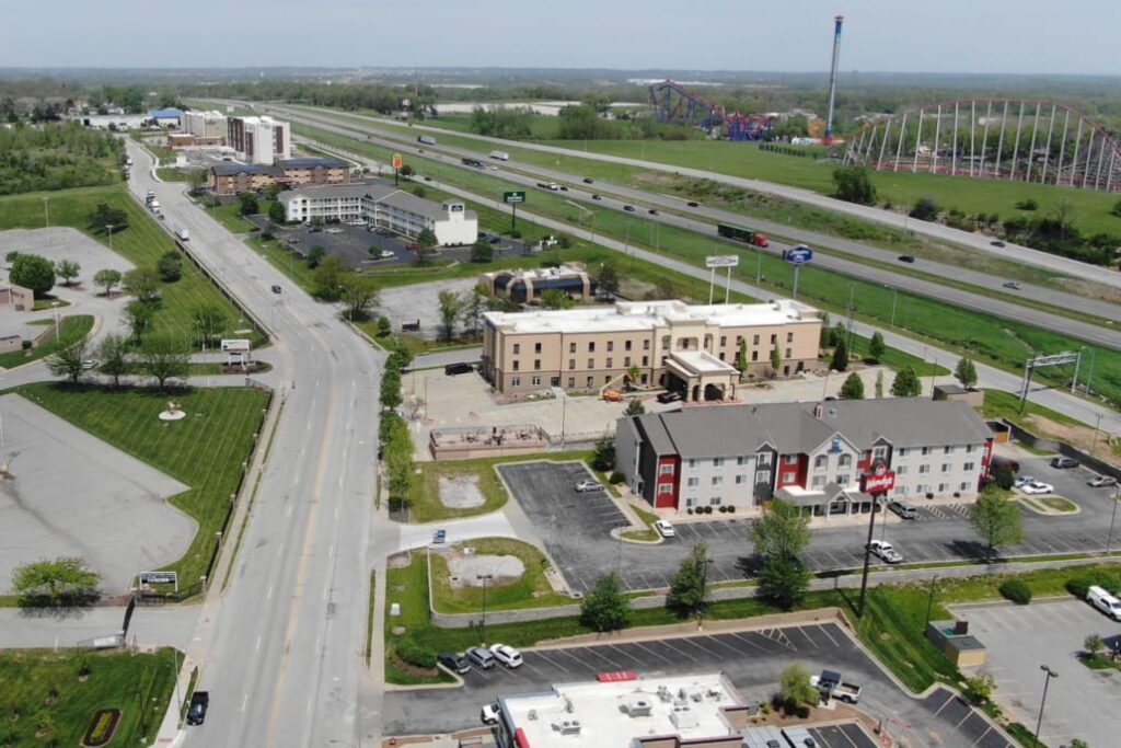 Hotels and commercial buildings along a main road with highway access, roller coasters, and rides visible in the distance.