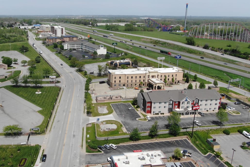 Aerial view of hotels and businesses along a highway, with cars on the road and roller coasters from an amusement park in the distance.
