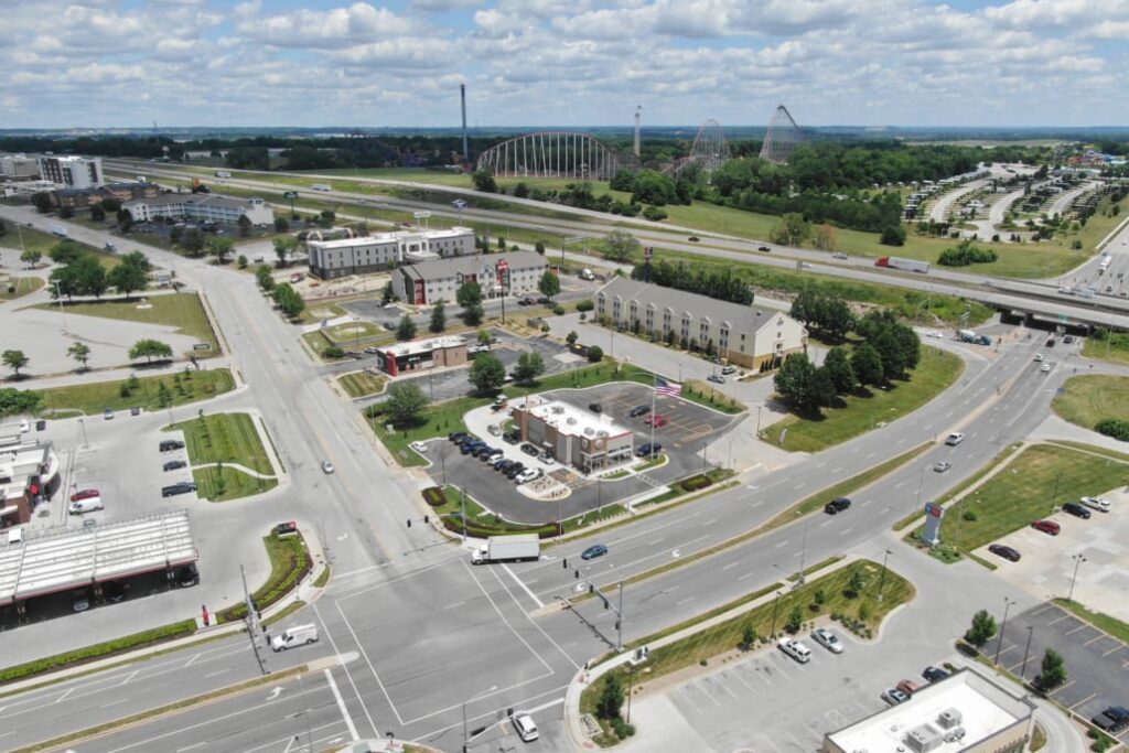 Intersection with commercial buildings, hotels, and restaurants, located beside a highway with roller coasters in the background.