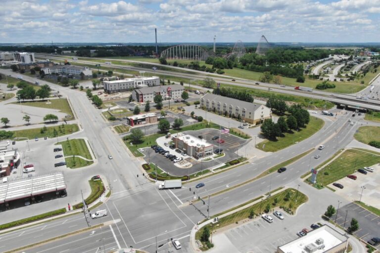 Intersection with commercial buildings, hotels, and restaurants, located beside a highway with roller coasters in the background.