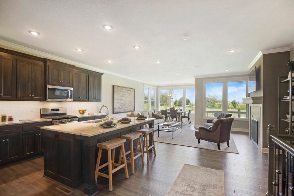 Spacious interior with dark wood kitchen cabinets, island seating, and adjoining living room featuring armchairs, dining area, and fireplace.