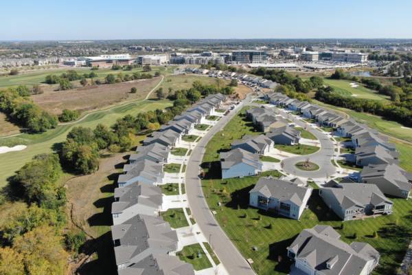 Curved rows of modern houses with gray roofs and green lawns, located beside a golf course with fairways and trees.