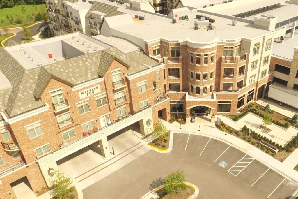 Aerial view of Mission 106 apartments featuring red-brick façades, a rounded corner tower, balconies, and landscaped entryways.
