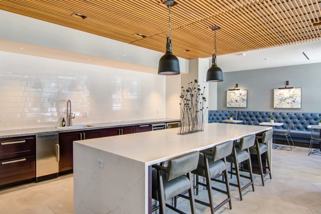 Spacious kitchen with a large marble island, bar stools, pendant lights, wood slat ceiling, and tufted booth seating along the wall.