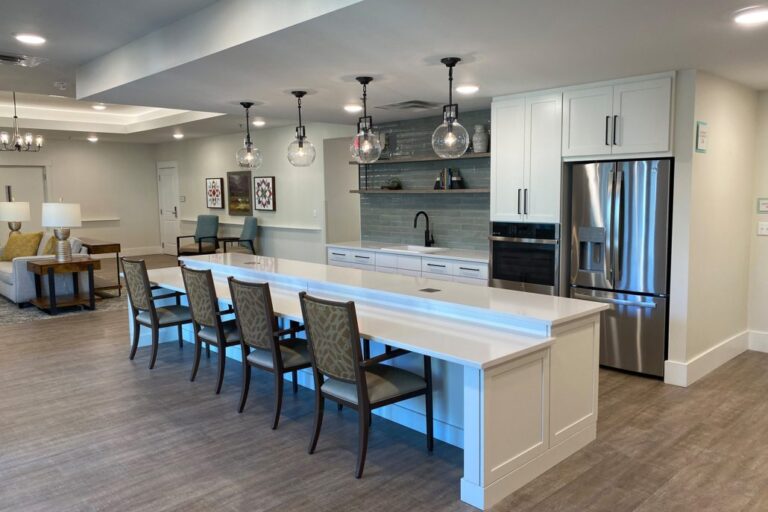 Spacious kitchen featuring a long white island with multiple chairs, stainless steel appliances, pendant lighting, and open shelving with decorative accents.