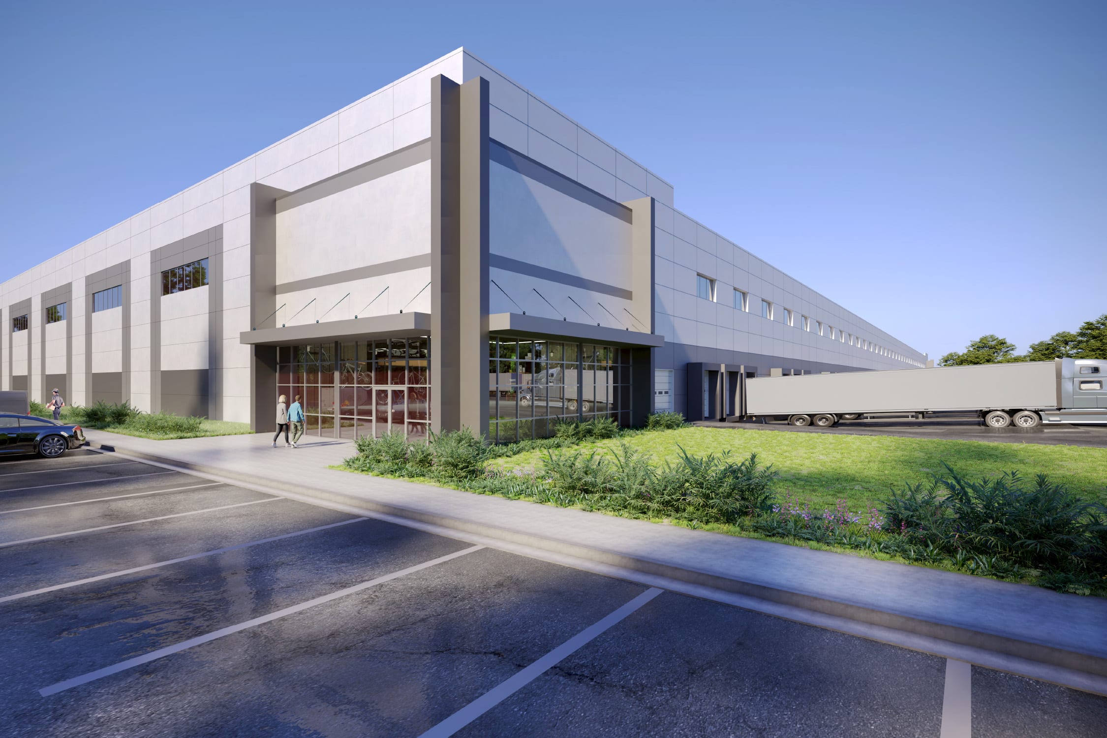 Large gray warehouse with glass entry, landscaped greenery, parking spaces, and a semi-truck parked at loading bays.