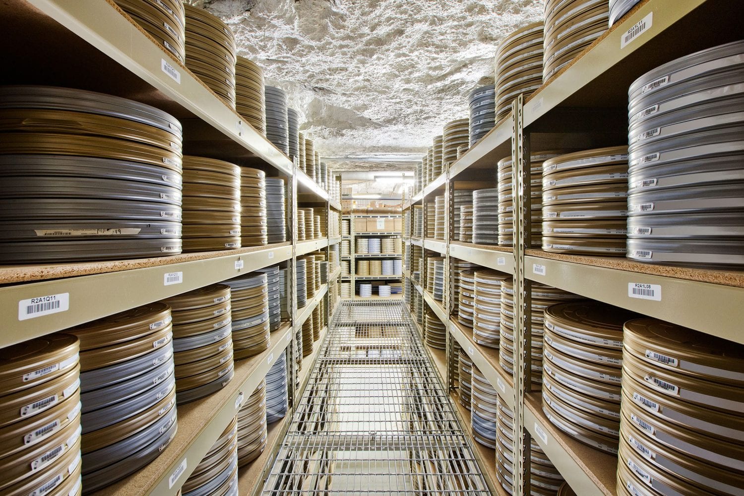Rows of metal shelves filled with neatly stacked film canisters in a climate-controlled underground storage room.